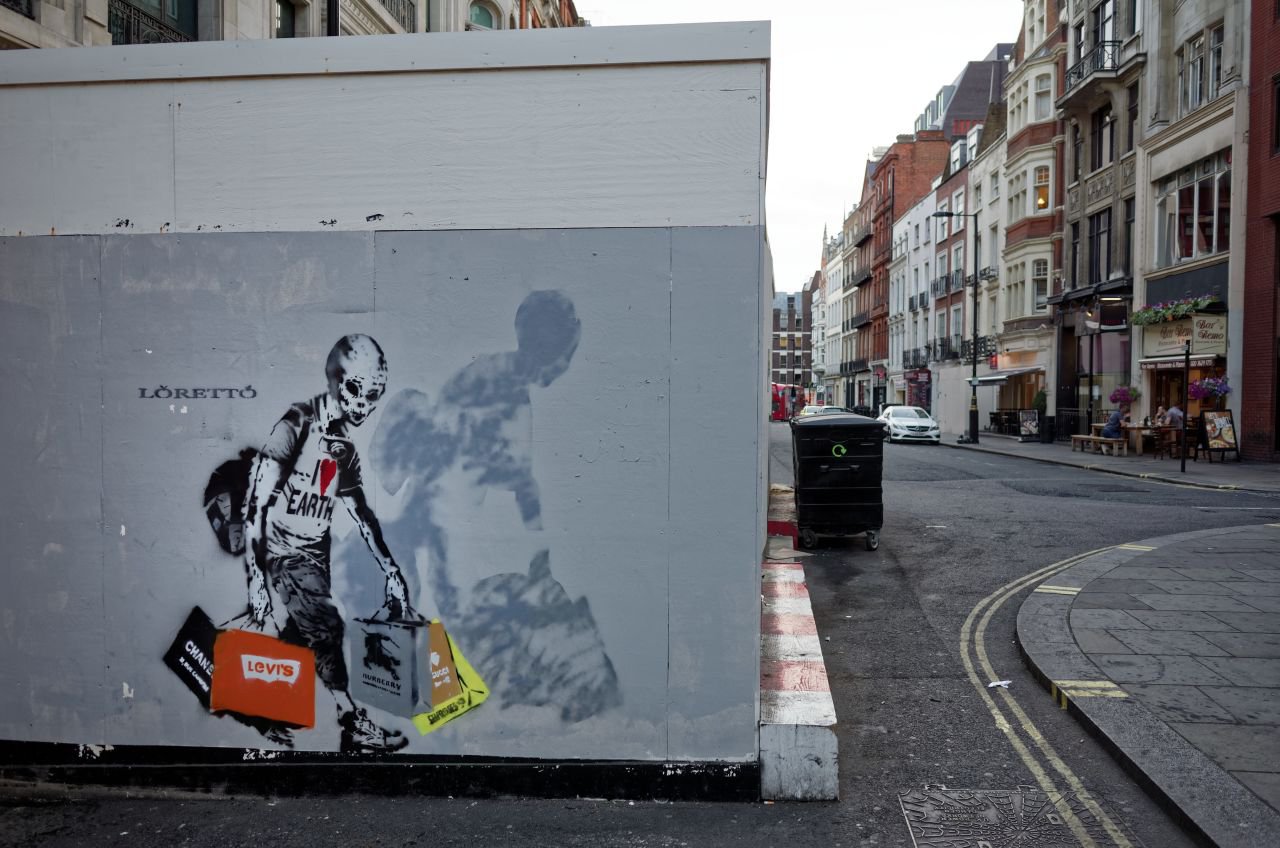 Street art depicting a skeleton wearing an I love earth t-shirt while carrying multiple branded shopping bags